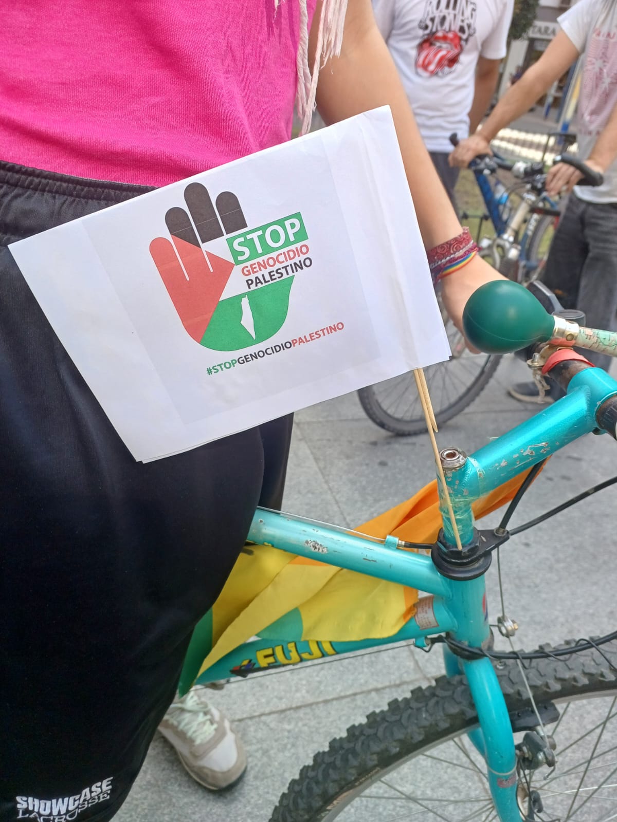 Fotografía de una bandera colocada en una bicicleta que pone: "Stop genocidio palestino" con un logo de la palma de una mano con los colores de la bandera palestina..